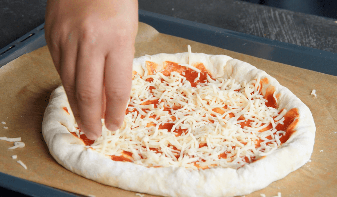 Pizzateig wird mit Tomatensauce und geriebenen Käse belegt