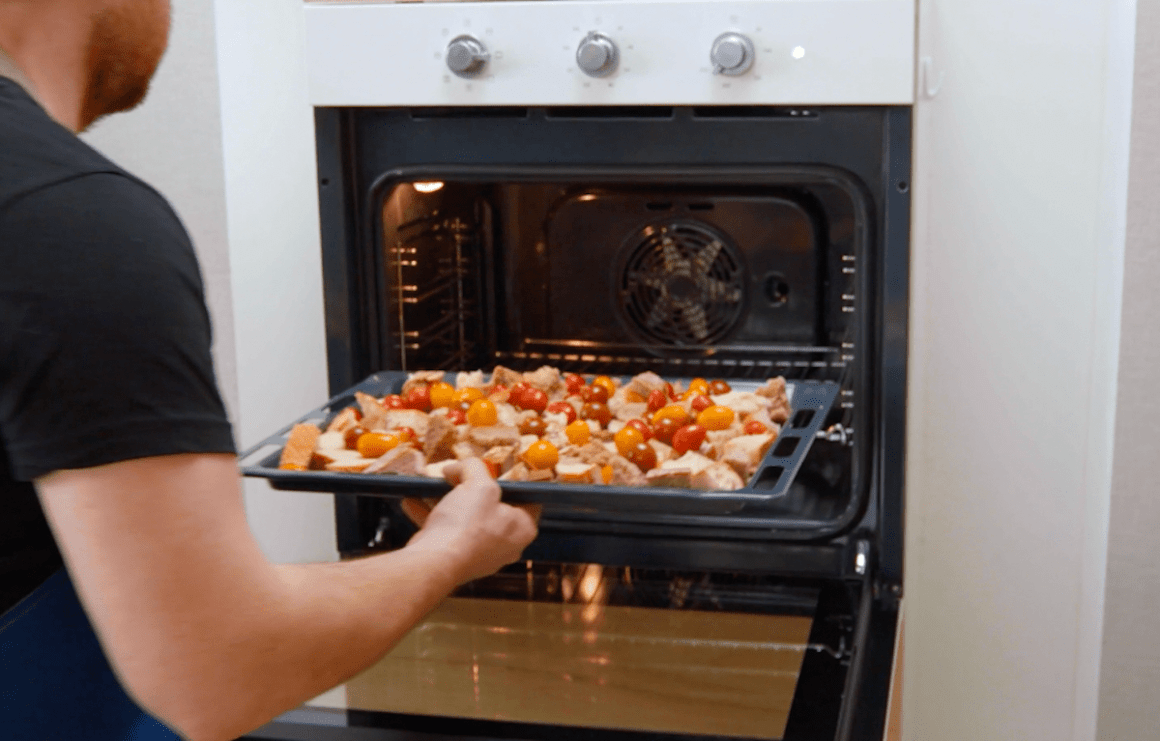 Brotwürfel und Kirschtomaten auf einem Backblech werden in einen Ofen geschoben